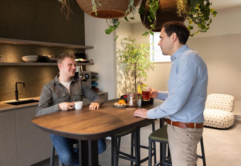 Twee collega's staan praten en lachend aan tafel
